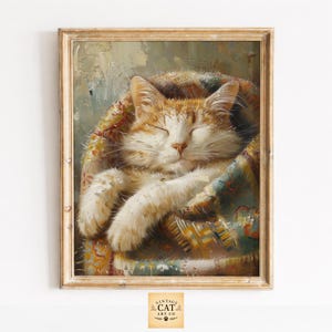 May include: A framed oil painting depicting an orange and white tabby cat with closed eyes, curled up and sleeping inside a colourful, textured blanket. The artwork features visible brushstrokes and a light-coloured wooden frame with the text Vintage Cat Art Co.