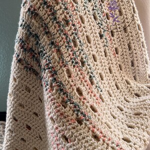 May include: Cream-colored crochet blanket with a textured pattern. The blanket features accents of pink and teal throughout the design. The Little Berry Crochet logo is visible in the upper right corner. The blanket is draped over a chair.