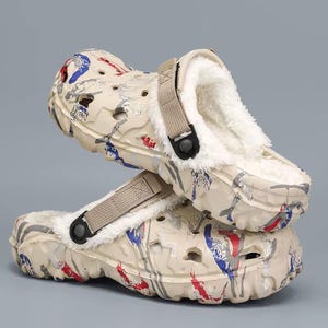 May include: Beige clogs with a white, fluffy interior and a strap. The clogs have a colorful pattern of red, blue, and gray paint-like strokes. The shoes are stacked on top of each other.