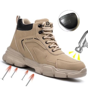 May include: A tan work boot with black detailing and a chunky sole. The boot has a lace-up closure and a reinforced toe cap. The image shows a diagram of a hammer hitting the boot and nails piercing the sole, highlighting its safety features.