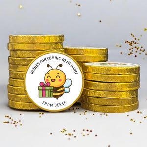 May include: A stack of round chocolate coins wrapped in gold foil. The top coin features a white sticker with a cartoon bee holding a green gift box with a pink bow. The text reads: THANKS FOR COMING TO MY PARTY FROM JESSE in black lettering.