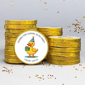 May include: Piles of gold-foil-wrapped chocolate coins. One coin has a label with a cartoon duck in a party hat, holding a gift. Text on the label says "THANKS FOR COMING TO MY PARTY" and "FROM SOFIA".