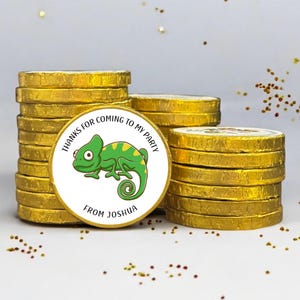 May include: A stack of round chocolate coins wrapped in shiny gold foil. The front coin features a white circular sticker with a green cartoon chameleon illustration and the black text: THANKS FOR COMING TO MY PARTY FROM JOSHUA.