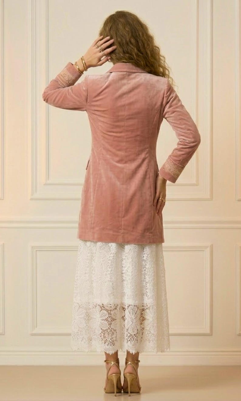 May include: A dusty rose velvet blazer with embroidered cuffs, paired with a white lace skirt. The outfit is completed with gold-colored high-heeled sandals. The ensemble is set against a neutral background.