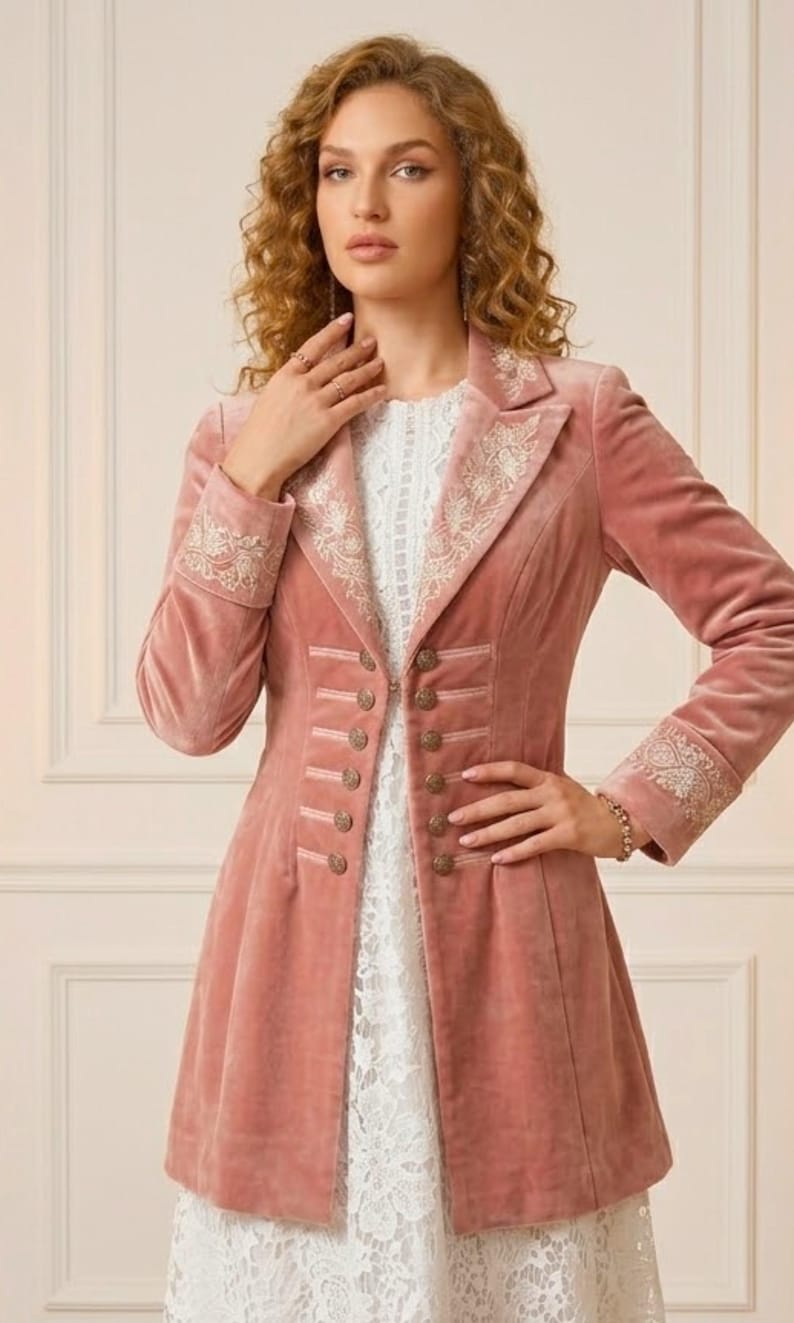 May include: A dusty rose velvet jacket with ornate embroidery on the collar and cuffs. The jacket features a tailored fit with decorative buttons and a flared skirt. The garment is worn over a white lace dress, creating a layered effect.