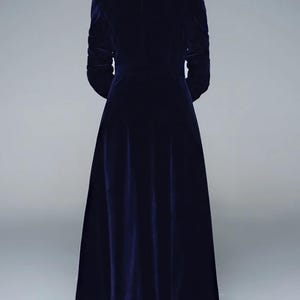 May include: A long, navy blue velvet coat with a tailored fit. The coat features a classic collar, long sleeves, and a floor-length hem. The back view showcases the coat's elegant design and luxurious fabric.