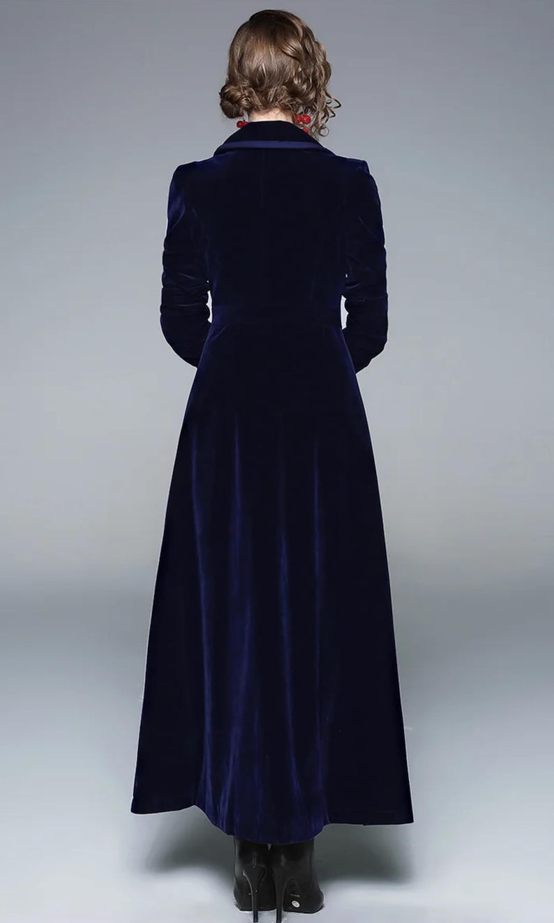 May include: A long, navy blue velvet coat with a tailored fit. The coat features a classic collar, long sleeves, and a floor-length hem. The back view showcases the coat's elegant design and luxurious fabric.
