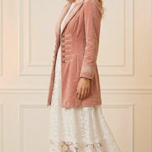 May include: A dusty rose velvet coat with ornate button details and embroidered cuffs. The coat is paired with a white lace dress and gold heels. The outfit is elegant and suitable for special occasions.