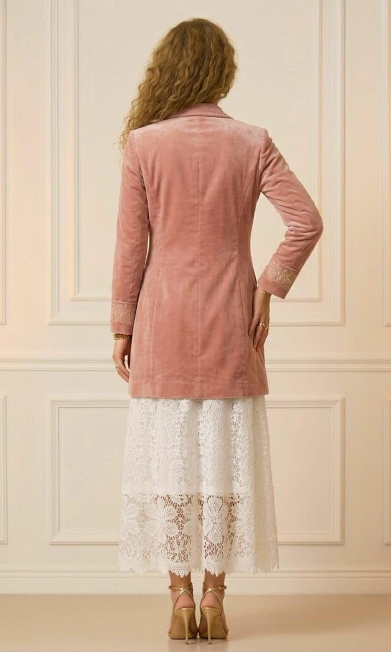 May include: A dusty rose velvet blazer with long sleeves and gold embroidered cuffs. The blazer is paired with a white lace skirt. Gold high heels complete the outfit, showcasing a sophisticated, feminine style.