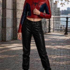 Puede incluir: Chaqueta de cuero corta roja y azul con un emblema de ara&ntilde;a negra en el pecho. La chaqueta se combina con pantalones de cuero negros y botas negras con cordones. El atuendo se usa al aire libre.
