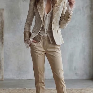 May include: Beige velvet blazer with gold embroidery, paired with matching trousers and a cream-colored blouse. The outfit is completed with lace-up boots. The ensemble is a sophisticated take on a classic suit.
