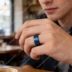 May include: A black ring with a blue geometric pattern. The ring is on a person's finger. The ring has a shiny finish and a dark blue interior. The ring is a piece of jewelry.