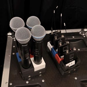 Puede incluir: Se muestran cuatro micr&oacute;fonos Shure Beta 58A con cabezales de malla plateada y cuerpos negros. Junto a ellos, varios receptores inal&aacute;mbricos negros con antenas. Los art&iacute;culos est&aacute;n sobre una superficie negra.