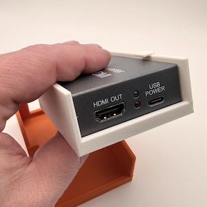 May include: A black HDMI converter with white and orange casing. The device has an HDMI OUT port and a USB POWER port. The text "HDMI OUT" and "USB POWER" are visible on the device.