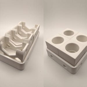 Puede incluir: Dos estructuras de cer&aacute;mica blanca. Una es una bandeja con m&uacute;ltiples compartimentos angulados. La otra es un bloque cuadrado con cuatro aberturas circulares, apilado sobre una bandeja similar. Ambas est&aacute;n en un entorno brillante y neutro.