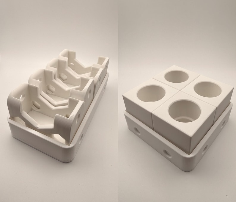 Puede incluir: Dos estructuras de cer&aacute;mica blanca. Una es una bandeja con m&uacute;ltiples compartimentos angulados. La otra es un bloque cuadrado con cuatro aberturas circulares, apilado sobre una bandeja similar. Ambas est&aacute;n en un entorno brillante y neutro.