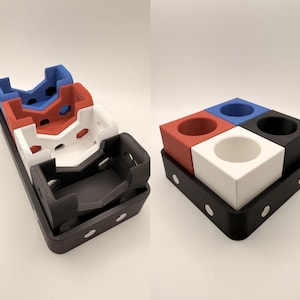 Puede incluir: Un conjunto de organizadores de escritorio multicolores de cuatro piezas, impresos en 3D. Los organizadores son rojos, blancos, azules y negros, y se asientan sobre una bandeja negra. La bandeja tiene detalles circulares blancos.