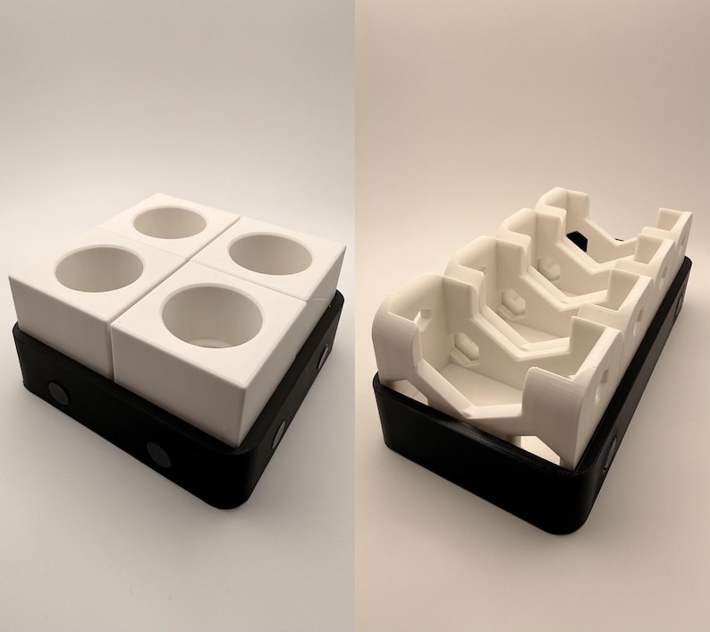 Puede incluir: Dos contenedores modulares geom&eacute;tricos blancos con aberturas circulares se asientan sobre una base rectangular negra. Los contenedores est&aacute;n dispuestos en forma cuadrada, con cuatro aberturas. Otra imagen muestra un contenedor geom&eacute;trico blanco con m&uacute;ltiples ranuras, tambi&eacute;n sobre una base negra.