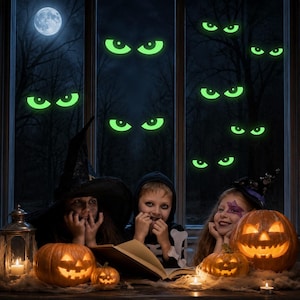 May include: Three children in costumes sit behind three carved jack-o'-lanterns and a book. The window behind them features glowing green eye decals against a dark night scene with a full moon, while lit candles sit on the table surface.