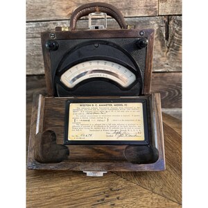 Puede incluir: Un amperímetro Weston D.C., modelo 45, vintage, en una caja de madera con asa de cuero. La esfera del medidor muestra "AMPERES D.C." con un indicador de aguja. La caja abierta revela una etiqueta con detalles técnicos y el número de serie 50674.