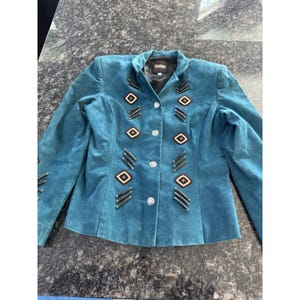 May include: Teal suede jacket with decorative diamond and bar accents. The jacket features a round collar, silver buttons, and black trim. A stylish outerwear piece.