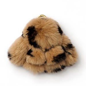 Puede incluir: Un llavero de piel sintética marrón y negra con un anillo de metal dorado. El llavero tiene un diseño en capas y un estampado de manchas, que se asemeja a un estampado de leopardo. El fondo es blanco.