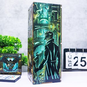 May include: A tall, rectangular wooden lamp featuring a vibrant, illuminated graphic of a figure in a dark coat and mask standing on a cobblestone street. The scene depicts a bridge and city architecture in shades of teal, green, and black.