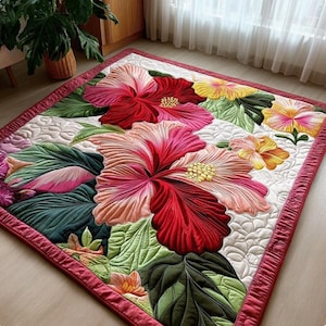 May include: A rectangular quilt featuring a vibrant floral pattern with large red, pink, and yellow hibiscus flowers and deep green leaves. The white background has a quilted texture, and the entire piece is bordered by a solid red fabric trim.