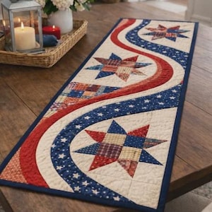 May include: A patriotic table runner with a cream background, red and blue wavy stripes, and star-shaped patchwork designs. The runner is bordered with a dark blue fabric and is placed on a wooden table.