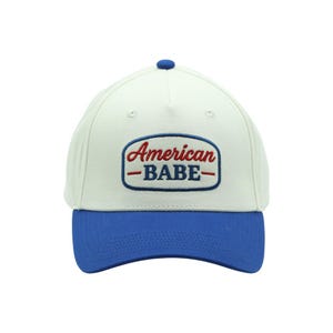 Può includere: Cappellino da baseball bianco con visiera blu e bottone blu. Il cappellino presenta la scritta ricamata "American BABE" in rosso e blu.