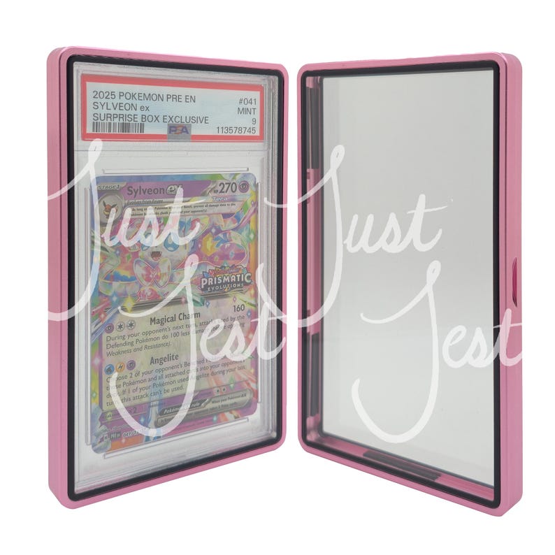May include: A pink protective case, open to reveal a Pok&eacute;mon trading card. The card features a Sylveon ex design with the text "Magical Charm" and "Prismatic Evolutions". The case has a black border and the text "2025 POKEMON PRE EN SYLVEON ex SURPRISE BOX EXCLUSIVE".