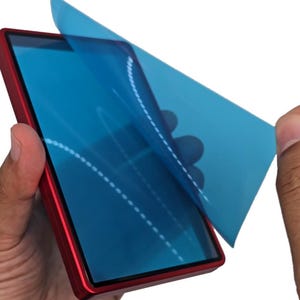 May include: A red smartphone with a blue screen protector being peeled off. The phone is held by two hands against a white background. The screen protector has a dotted design.