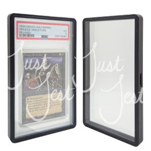 May include: A graded Magic: The Gathering card, "Drudge Skeletons," from the Revised edition, encased in a black protective holder. The card features skeletal figures and text. The holder is displayed next to an empty holder.
