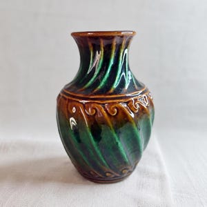 Peut inclure: Un petit vase décoratif en céramique avec une finition brillante. Le vase présente un motif tourbillonnant dans les tons de vert et de marron, avec un bord détaillé. Le vase mesure environ 15 cm de haut.