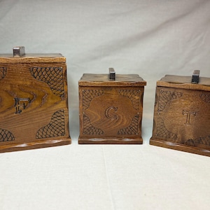Peut inclure: Trois boîtes de rangement en bois avec couvercles. Les boîtes sont de couleur marron chaud et présentent des détails décoratifs sculptés et les lettres "F", "C" et "T". Chaque boîte a une petite poignée sur le dessus.