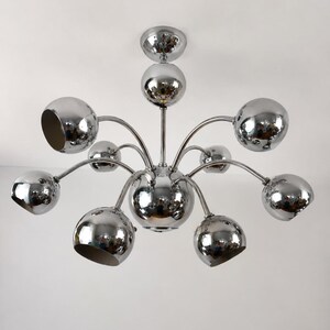 Peut inclure: Un lustre chromé avec une sphère centrale et de multiples bras incurvés, chacun portant un luminaire sphérique. Le métal poli reflète l'environnement, créant un luminaire moderne et élégant.
