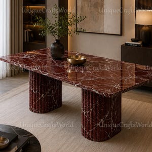 Peut inclure: Une table à manger rectangulaire dotée d'un plateau en marbre rouge profond poli avec des veines blanches. La table est soutenue par deux bases cylindriques cannelées substantielles fabriquées dans le même marbre rouge.