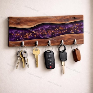 May include: A wooden key holder with a purple and gold resin inlay. The key holder has five silver hooks with various keys hanging from them. The wood has a natural grain pattern.