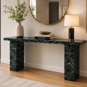 Può includere: Un tavolo console rettangolare con finitura in marmo verde scuro e venature bianche, sostenuto da due spesse gambe a lastra di marmo abbinate. La superficie del tavolo ospita un vaso bianco a coste con vegetazione, una ciotola dorata e due libri.
