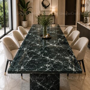 Peut inclure: Une table à manger rectangulaire dotée d'un plateau en marbre vert foncé avec des veines blanches et d'un pied central assorti. La table est entourée de six chaises rembourrées en tissu crème, avec des dossiers incurvés et des pieds sombres.