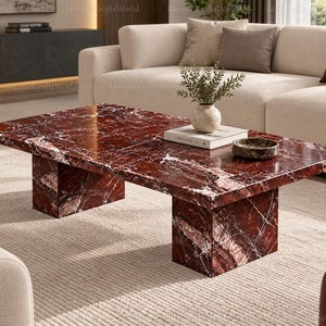 May include: A rectangular coffee table crafted from deep red marble with prominent white veining. The table features a smooth, polished surface and is supported by two thick, matching marble block legs, creating a solid and uniform appearance.