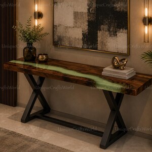 May include: A wooden console table with a live edge design and a green resin river. The table has black metal X-shaped legs. Decorative items, including a vase with greenery, are on the table.
