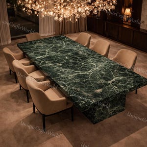 Può includere: Un grande tavolo da pranzo rettangolare con piano in marmo verde scuro e base abbinata. Otto sedie imbottite beige circondano il tavolo. Sopra il tavolo è appesa un lampadario decorativo con globi di vetro. Il testo "UniqueCraftsWorld" è visibile.