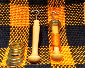 May include: Two wooden yarn winders with metal hooks on a black and orange checkered fabric. One winder has orange yarn wound around it. The other winder has a stack of metal washers next to it.