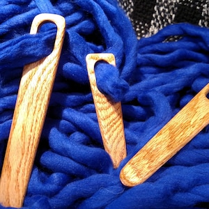 May include: Three wooden knitting needles with different sized loops, lying on a blue fuzzy surface.