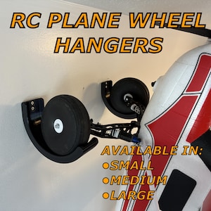May include: Black RC plane wheel hangers mounted on a wall, holding a plane's wheels. The text "RC PLANE WHEEL HANGERS" is at the top. Below, the text reads "AVAILABLE IN: SMALL, MEDIUM, LARGE."