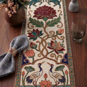 Könnte beinhalten: Perlen-Tischläufer mit cremefarbenem Hintergrund und aufwendigen Blumen- und Vogelmotiven. Der Läufer hat ein zentrales Blumenmotiv mit blauen und grünen Akzenten und eine Bordüre aus blauen, grünen und goldenen Perlen. Das Design umfasst Einhörner, Blumen und Vögel.