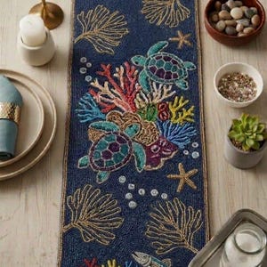 May include: A navy blue beaded table runner with an underwater theme. The runner features sea turtles, coral, starfish, and fish in various colors. Gold-colored seaweed-like designs are also present. The runner is rectangular in shape.
