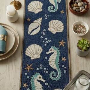 May include: A rectangular table runner featuring a deep blue beaded background with a pattern of white seashells, light blue and white seahorses, gold starfish, and small white bubbles. The edges are finished with a gold beaded border.