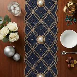 Può includere: Un runner da tavola rettangolare con una superficie di perline blu navy scuro, un intricato motivo geometrico a reticolo dorato e tre grandi perle artificiali bianche centrate. Il runner presenta un bordo smerlato e un design simmetrico.